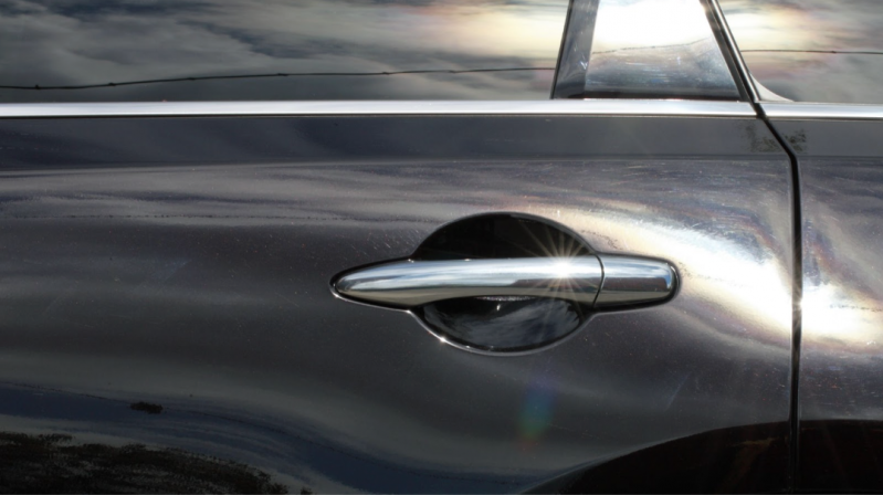 汽車鍍鉻門把手特寫，陽光照射在黑色鏡面車漆上形成強烈反光，展現車身塗層的質感